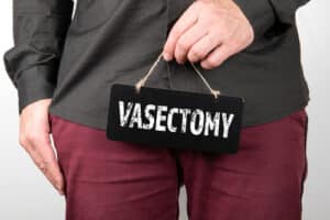 A man holding a Black chalk board with text Vasectomy