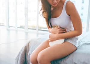 Shot of an unrecognizable woman holding her stomach in pain with a hot water bottle in her bedroom during the day